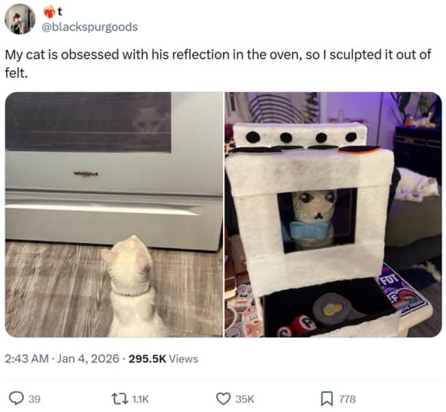 White cat staring at oven reflection next to handmade felt toy oven sculpture.