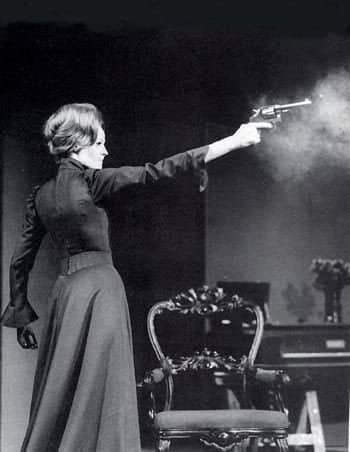 Vintage black and white photo of woman firing revolver indoors with dramatic smoke.