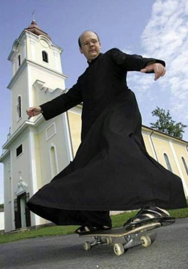 Priest in long black cassock and sandals riding skateboard in front of church.