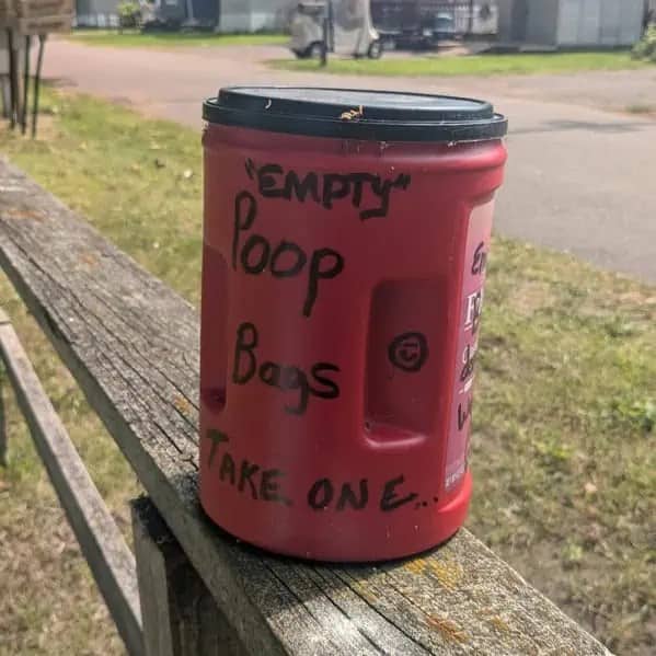Red outdoor container labeled empty poop bags with unnecessary quotes placed around empty.