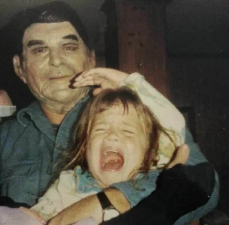 Old school cool photo of a stoic grandfather holding a crying toddler indoors.