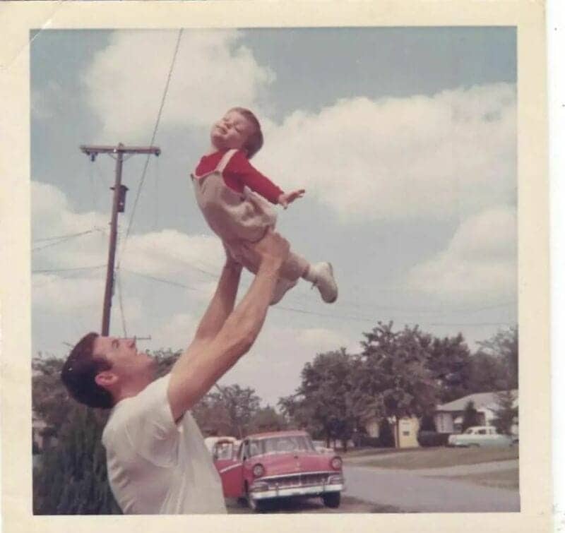 Old school cool father tossing his young toddler high into the air outside.