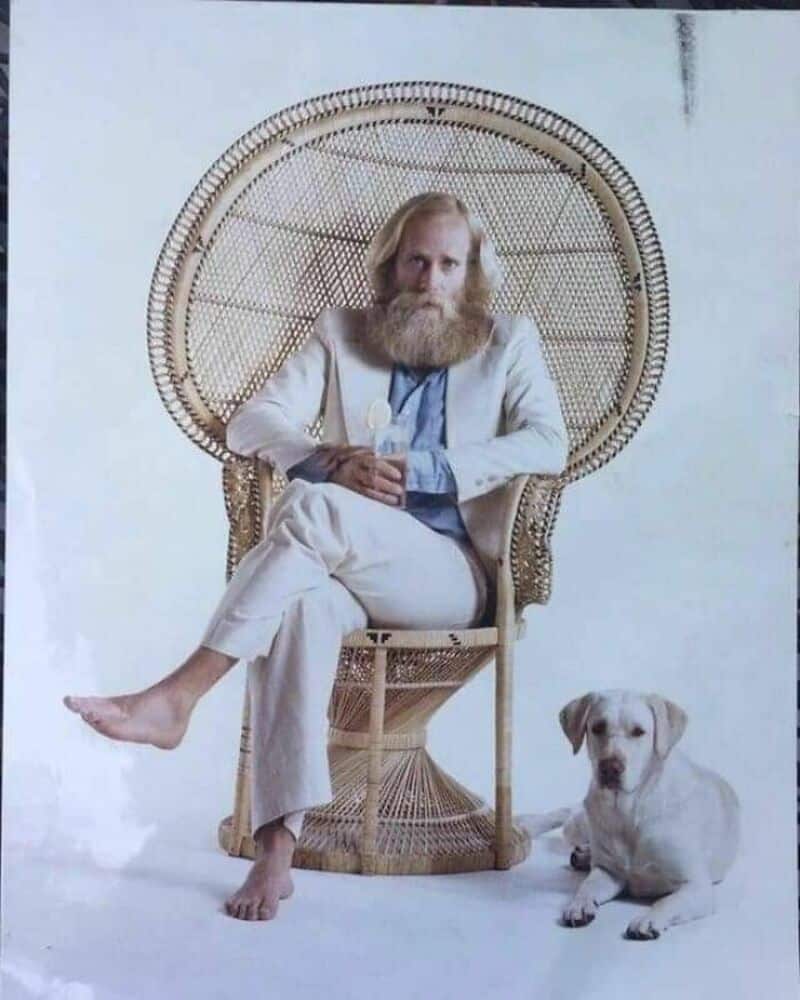 Old school cool bearded man sitting barefoot in a peacock chair with dog.
