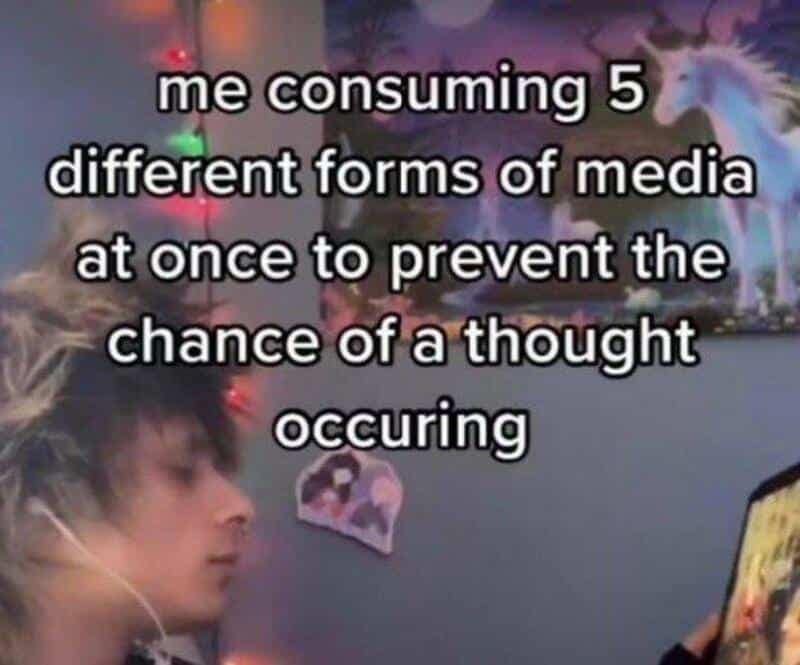 Image of a person sitting in a dark bedroom wearing headphones while staring at a tablet, captioned about consuming five forms of media simultaneously to prevent inner thoughts.