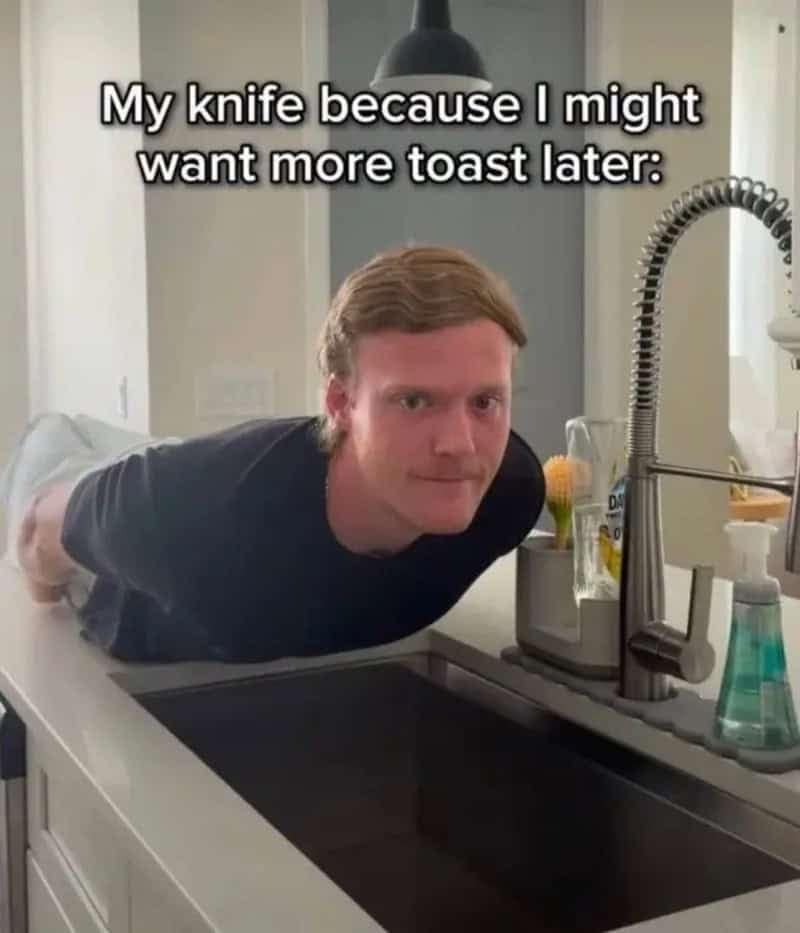A man planking across a kitchen counter over the sink while staring into the camera, representing a butter knife left on the edge of the sink in case of more toast later.