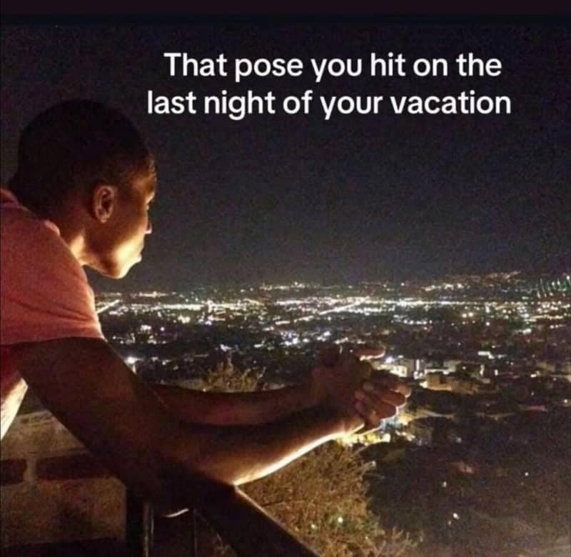 A man leaning solemnly over a balcony railing at night overlooking city lights in a relatable meme about reflecting on the final night of a vacation.