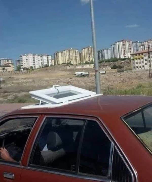 A red car outfitted with a full residential house window installed as a DIY sunroof.