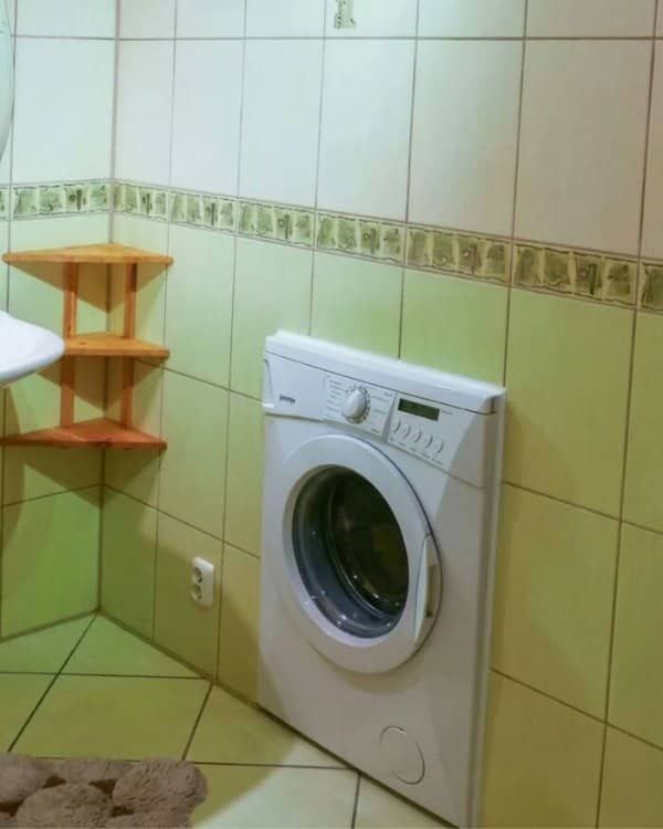 A front-loading washing machine mounted directly into a tiled bathroom wall to save space.