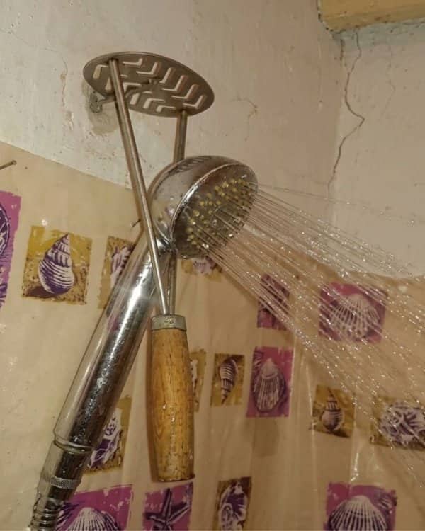 A showerhead supported in place using a stainless steel potato masher fixed to the wall.