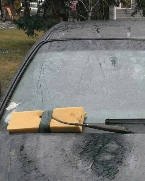 A car windshield wiper arm modified with a large yellow sponge taped in place.
