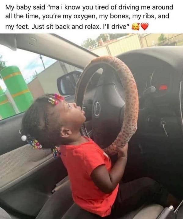 Small toddler sitting behind a car steering wheel pretending to drive her mother around.
