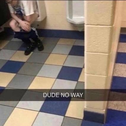 Person sitting completely on a public bathroom urinal as if using a toilet.