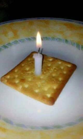 Sad miniature birthday celebration consisting of one square saltine cracker topped with a lit candle.