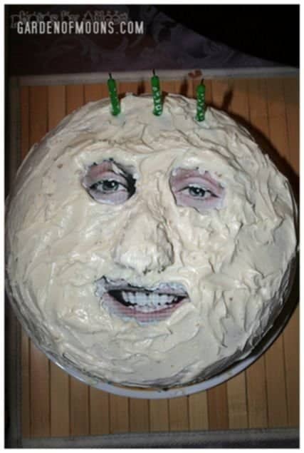 Terrifying round birthday cake covered in white frosting with a printed human face peeking through.