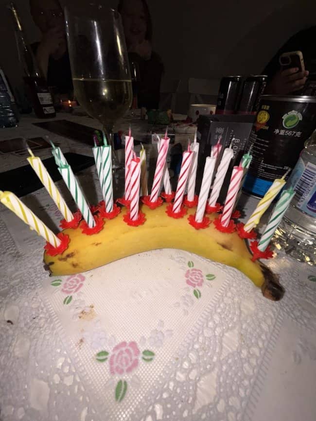 Unpeeled yellow banana acting as a makeshift birthday cake covered in brightly lit striped candles.