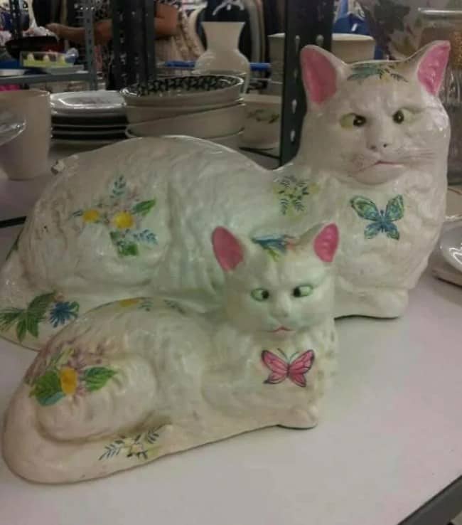 Unsettling ceramic thrift store find showing two cross-eyed white cats decorated with colorful painted butterflies.