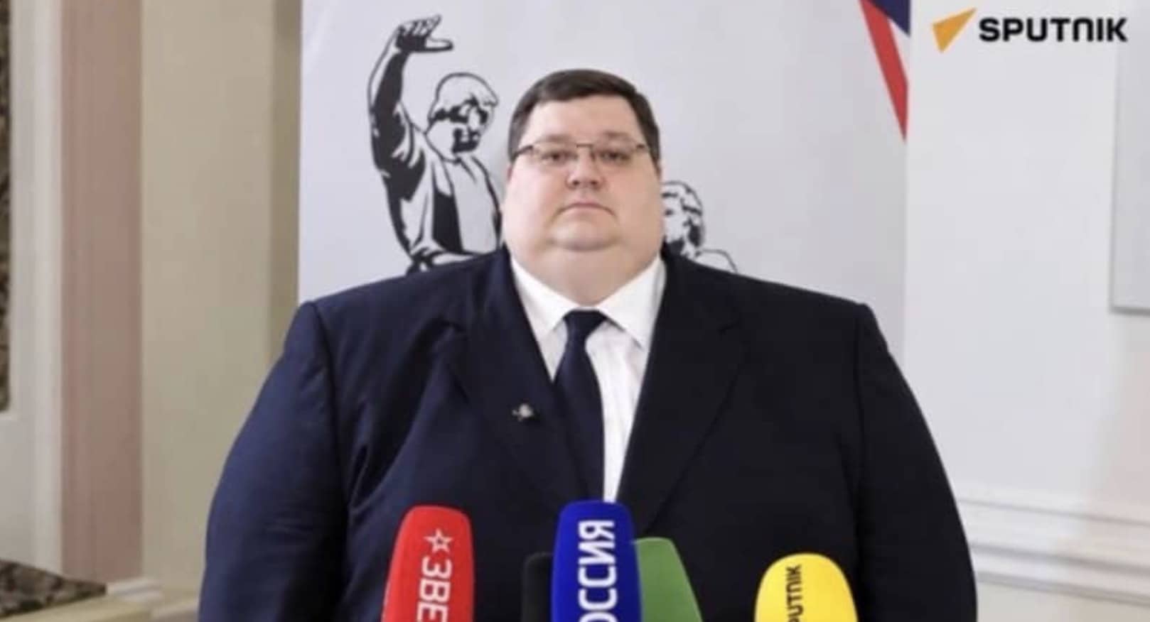 Large man in a suit standing at a press conference microphone for funny memes.