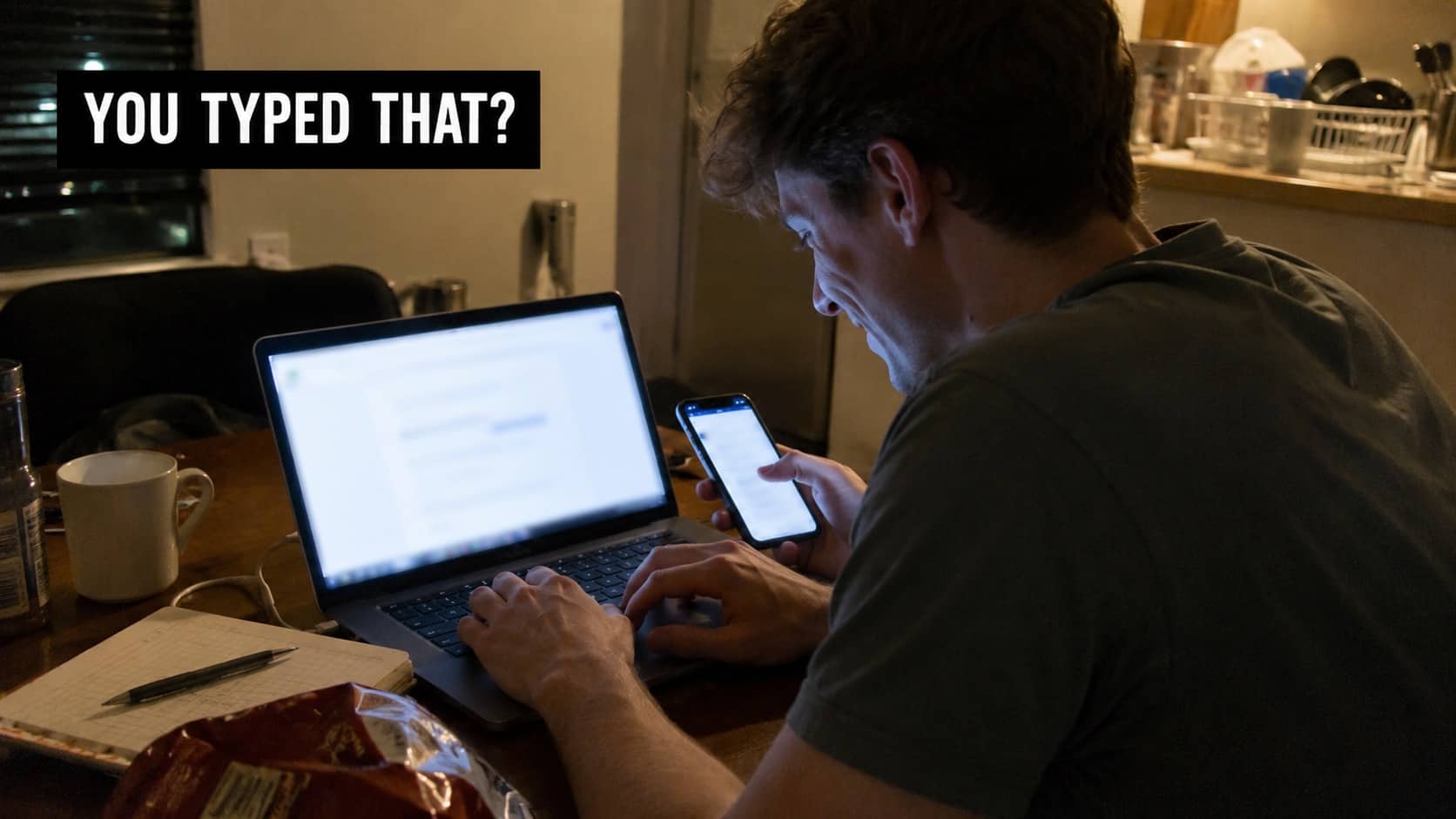 Young man using a smartphone and typing on a laptop computer in a dark room.