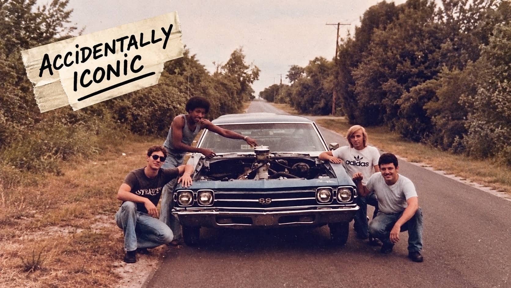 Four men posing with an open hood classic muscle car parked on a road.