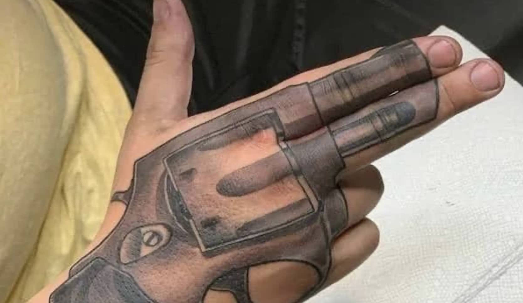 Tattoo of a revolver hand gun positioned over a person's hand and extended fingers.