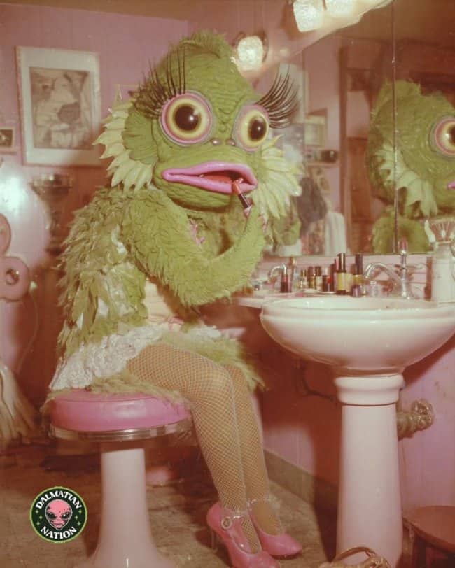 Green swamp monster in fishnets and vanity chair applying lipstick retro humor 50s memes.
