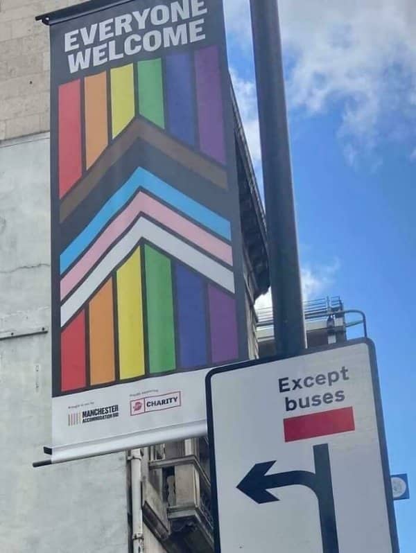 Pride banner reading everyone welcome hangs directly above a road sign reading except buses.