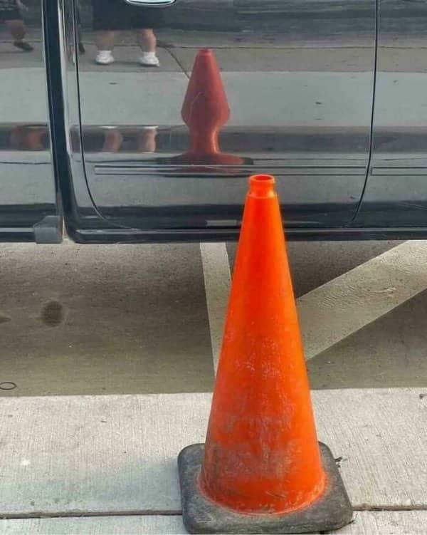 An orange traffic cone reflects in a car door and distorts into an unfortunate shape.