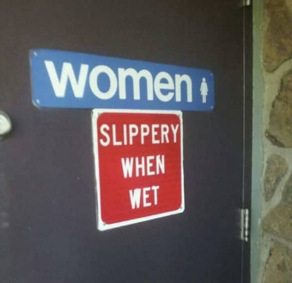 A women's restroom door sign sits directly above a red slippery when wet warning.