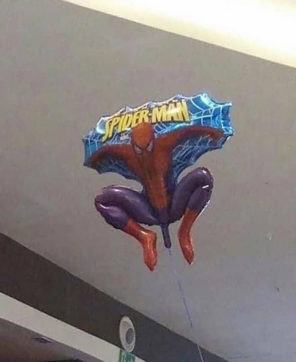 A Spider-Man foil balloon floats against a ceiling in an unfortunately arranged crouching pose.