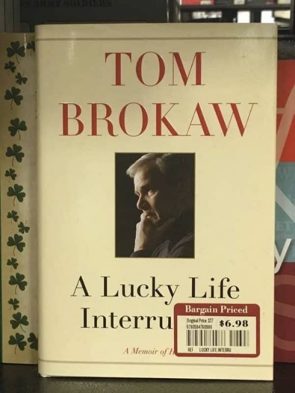 A price sticker covers part of a Tom Brokaw memoir title on a bookshop shelf.