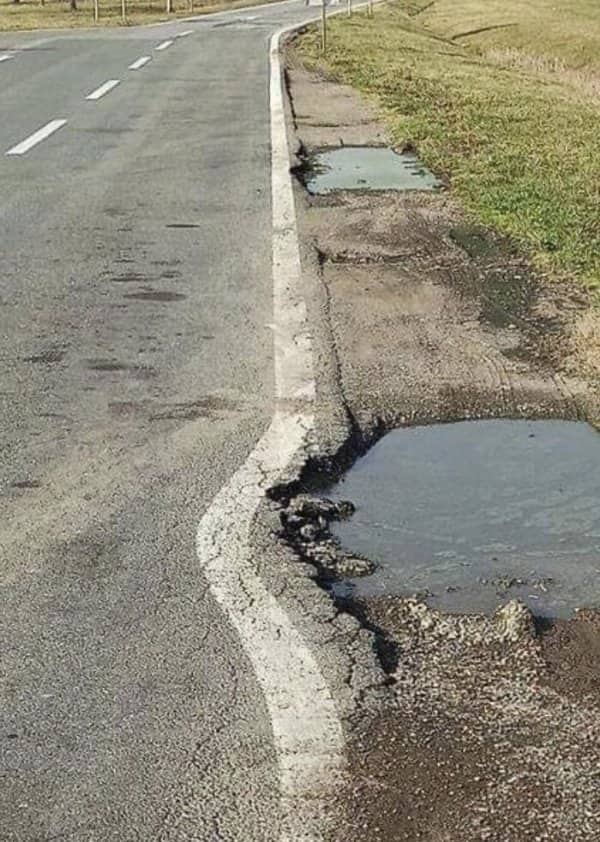 Balkan road meme displaying painted lane line bending around deep water filled potholes along asphalt.