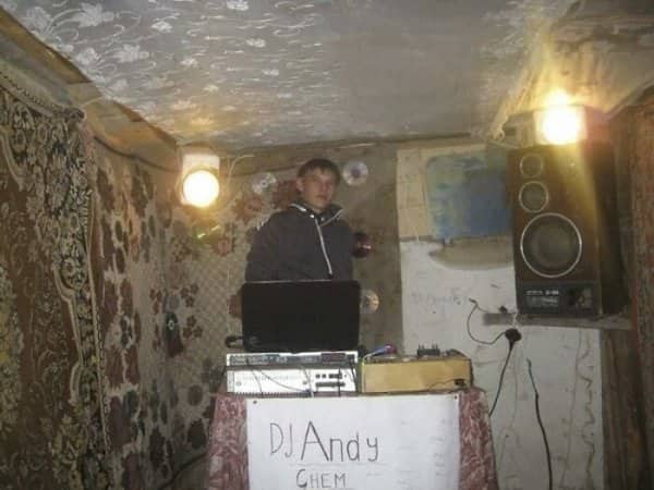 DJ Andy performing with laptop and speakers inside room covered with traditional Balkan carpets.