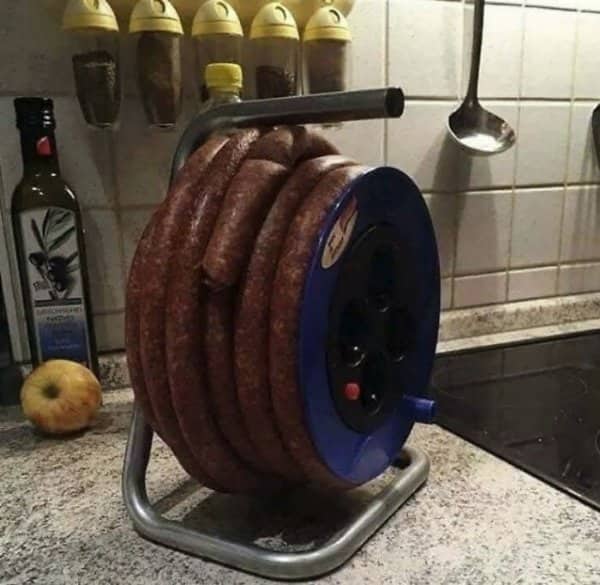 Coiled smoked sausage wrapped around blue cable reel stand on kitchen counter Balkan meme.