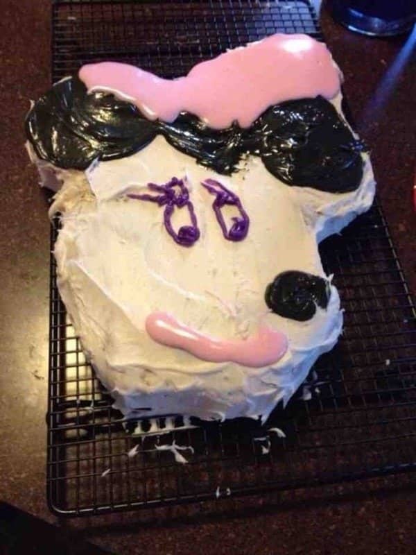 Sheet cake decorated as an animal face with black ears, a pink bow and purple piped eyes
