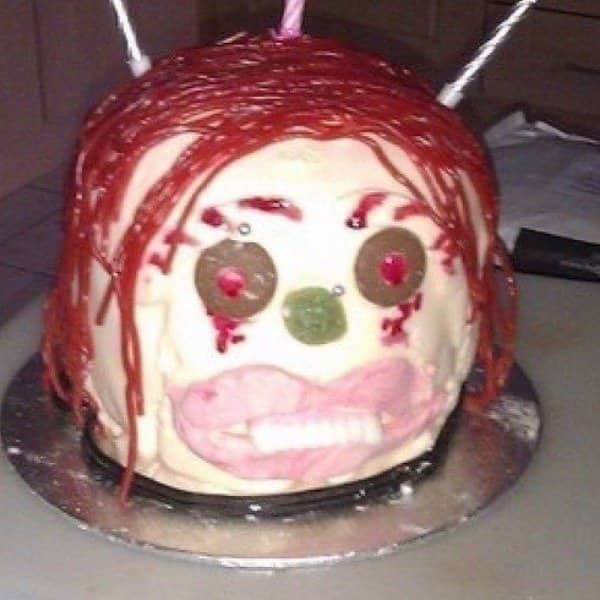 Round cake decorated as a face with stringy red icing hair and mismatched candy eyes