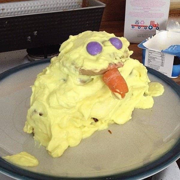 Yellow cake melted into a puddle with purple candy eyes and a carrot beak