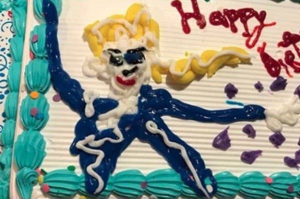 Sheet cake with a blue piped figure and yellow hair sprawled across a birthday message