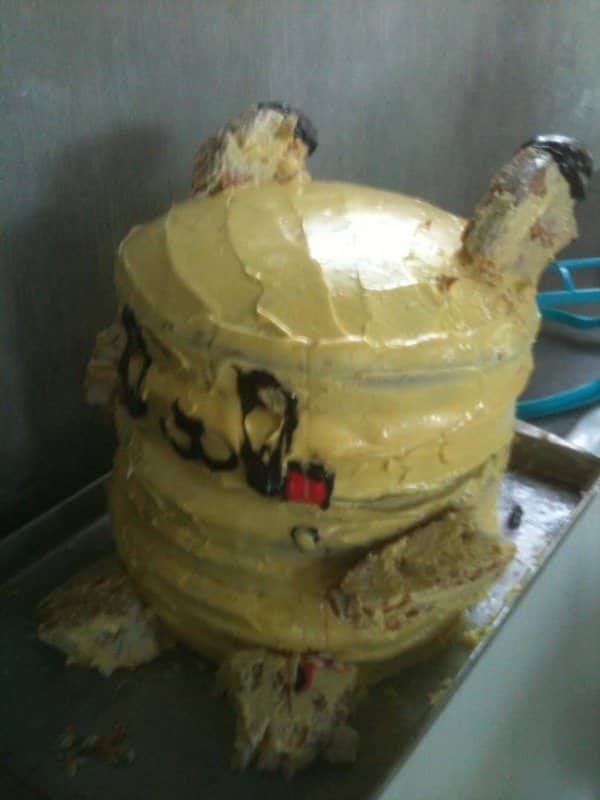 Yellow frosted cake collapsing off a tray with crumbling ears and smeared black details