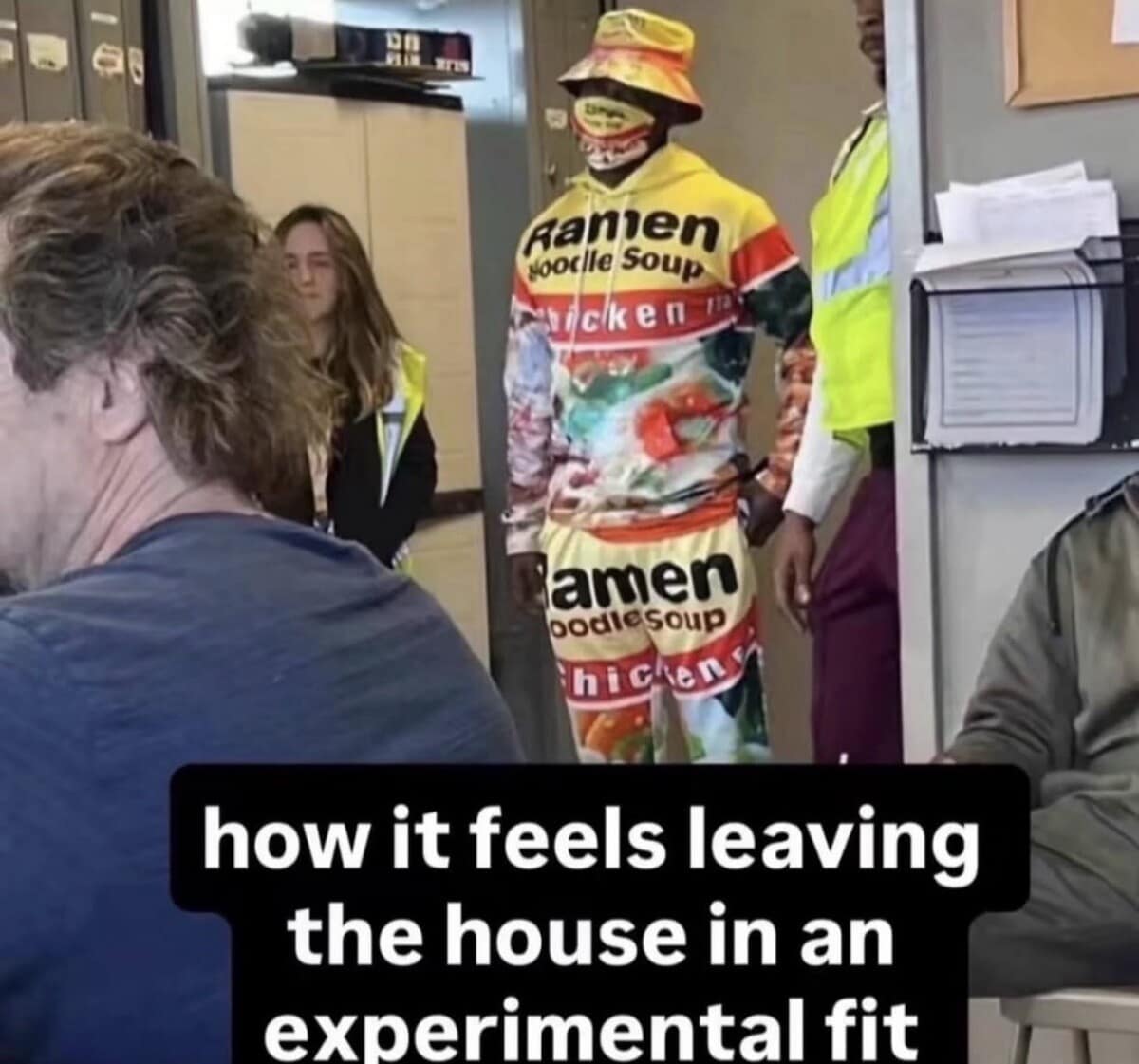 Person standing in an office wearing a head-to-toe chicken ramen noodle soup track suit, bucket hat, and mask, captioned about wearing an experimental fit in a classic meme.