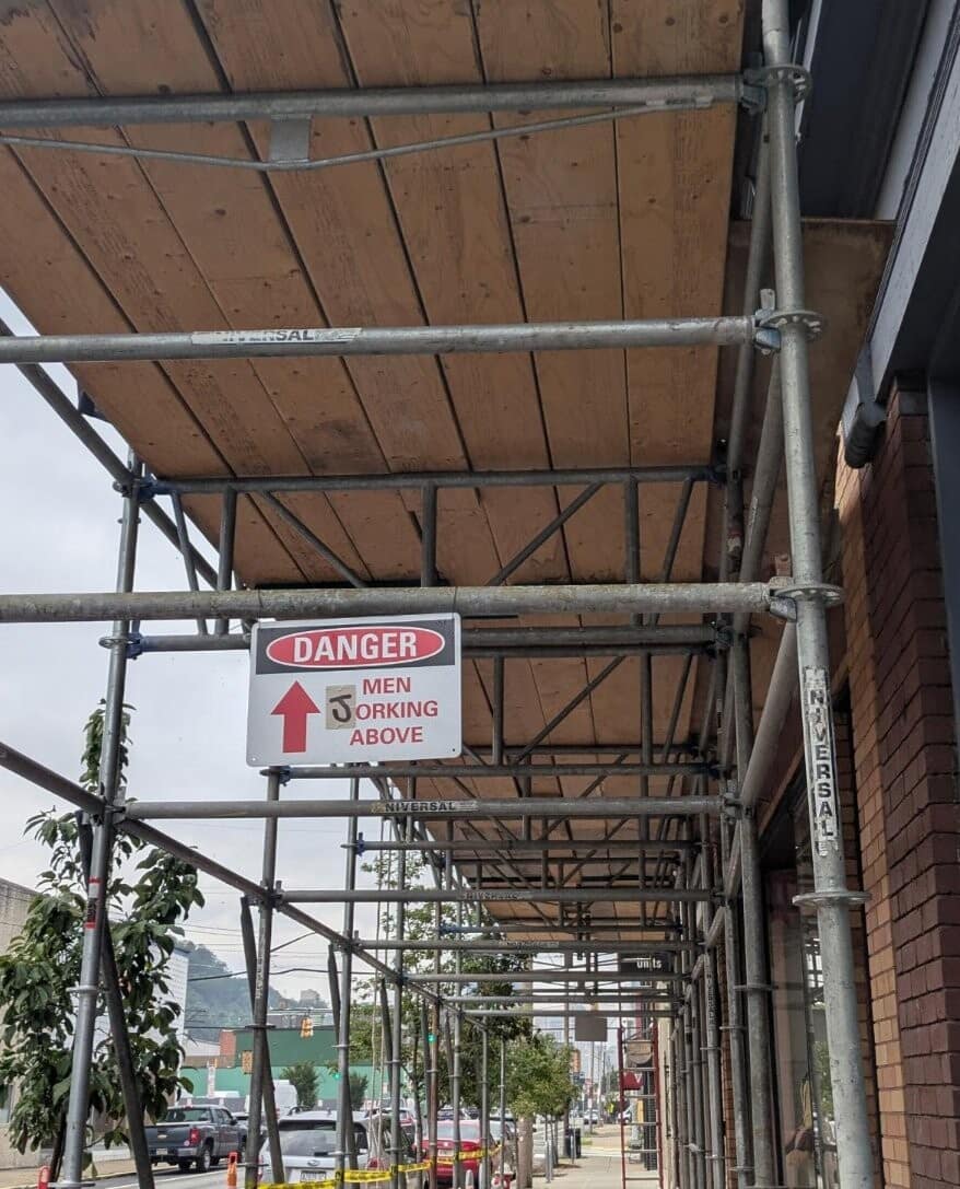Urban construction scaffolding warning sign altered to read 'DANGER MEN JORKING ABOVE' in a classic meme.