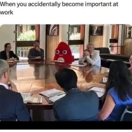 Red bean-like corporate mascot sitting awkwardly in a formal boardroom meeting surrounded by executives, shared in a classic meme.