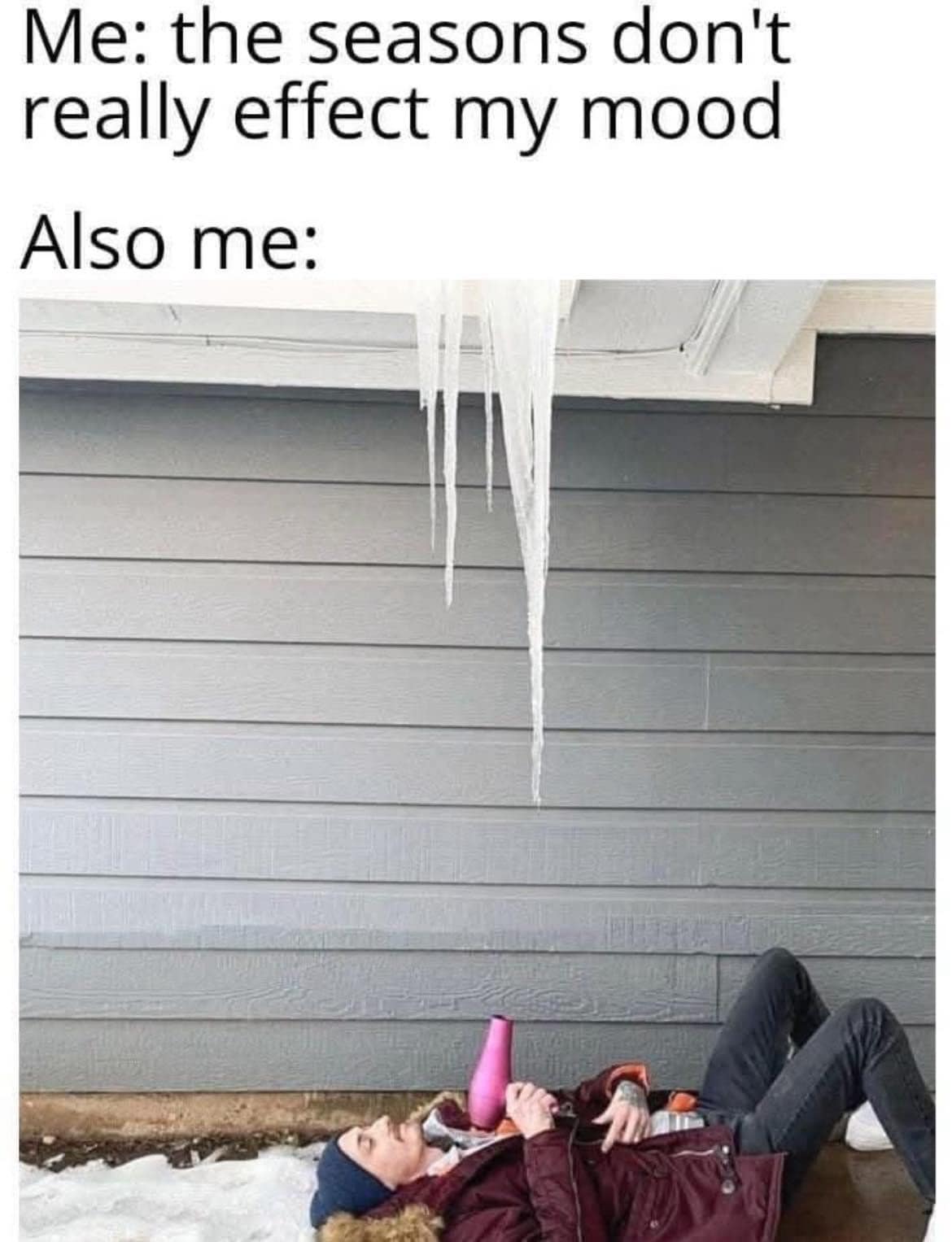 Man lying in snow trying to melt a massive roof icicle using a pink handheld hair dryer in a classic meme about winter moods.