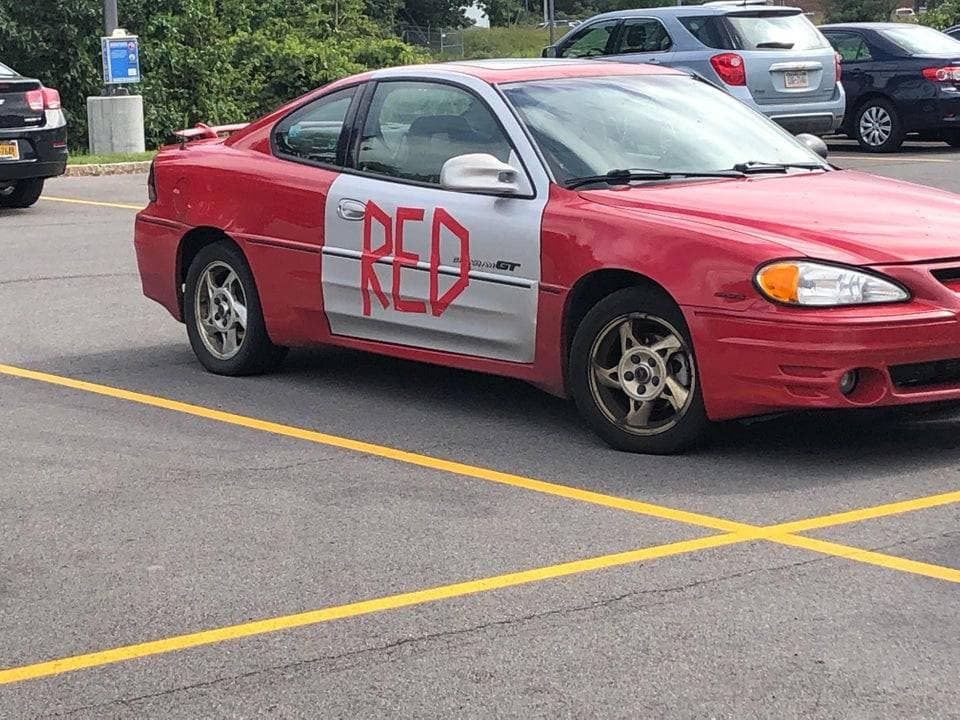 Red car with a mismatched silver replacement door that has the word 'RED' spray-painted onto it in an old memes photo.