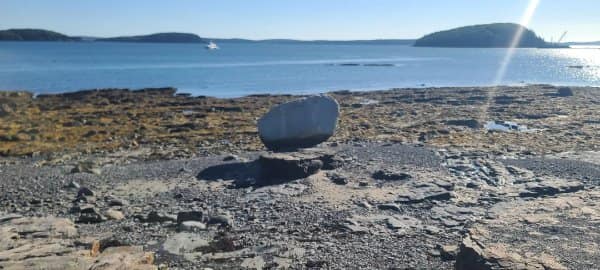 Rock sitting on a rocky beach at low tide that appears to float above the ground.