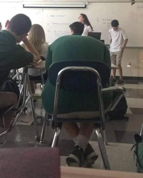 Classroom photo where a student's green hoodie merges with a chair into a giant torso.
