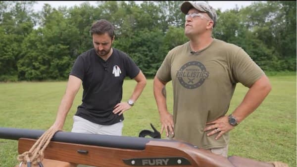 Man touching a rifle stock that seems to grow out of another man's belly.