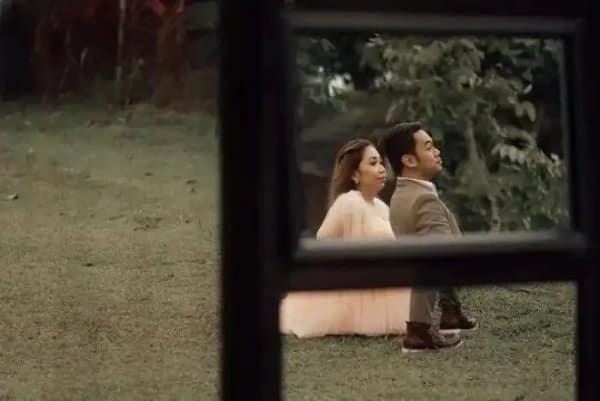 Couple posing outside a window frame that cuts their bodies into strange proportions.