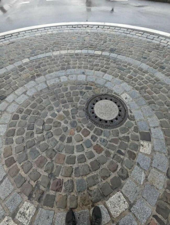 Cobblestone circle built around a manhole cover set noticeably off center.
