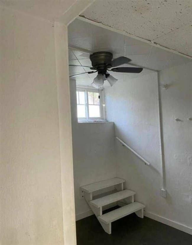 Small room with a ceiling fan hung so low over a short set of stairs.