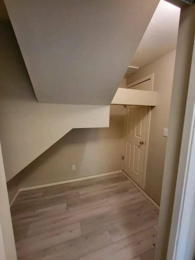 Finished basement room where the underside of a staircase crowds most of the space.